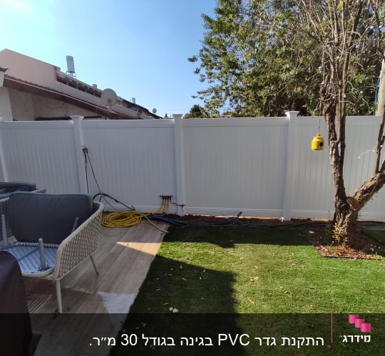גינה עם דשא סינתטי, עץ, גדר לבנה וצינור צהוב